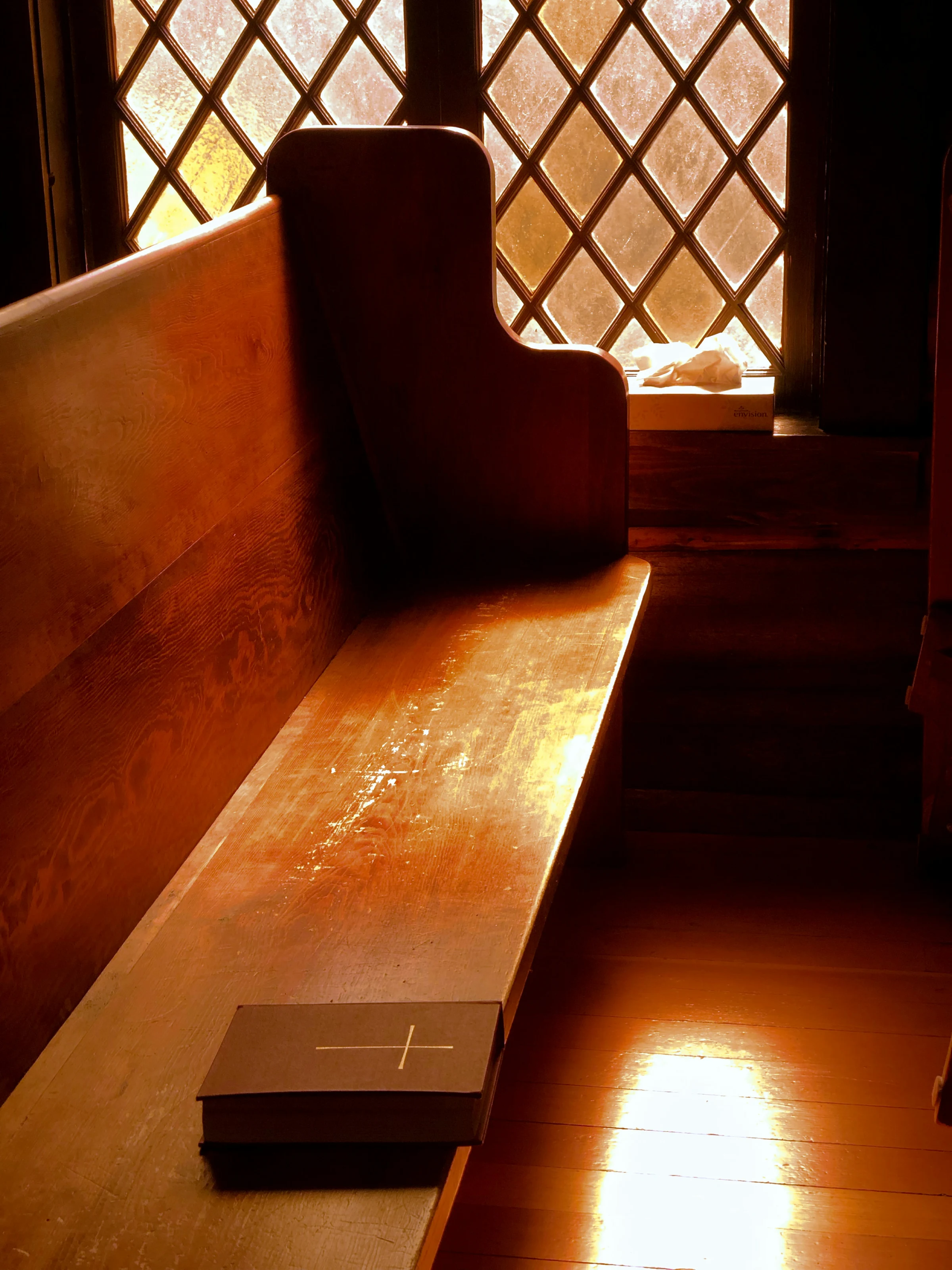 A hymnal at rest on an empty wooden church pew.