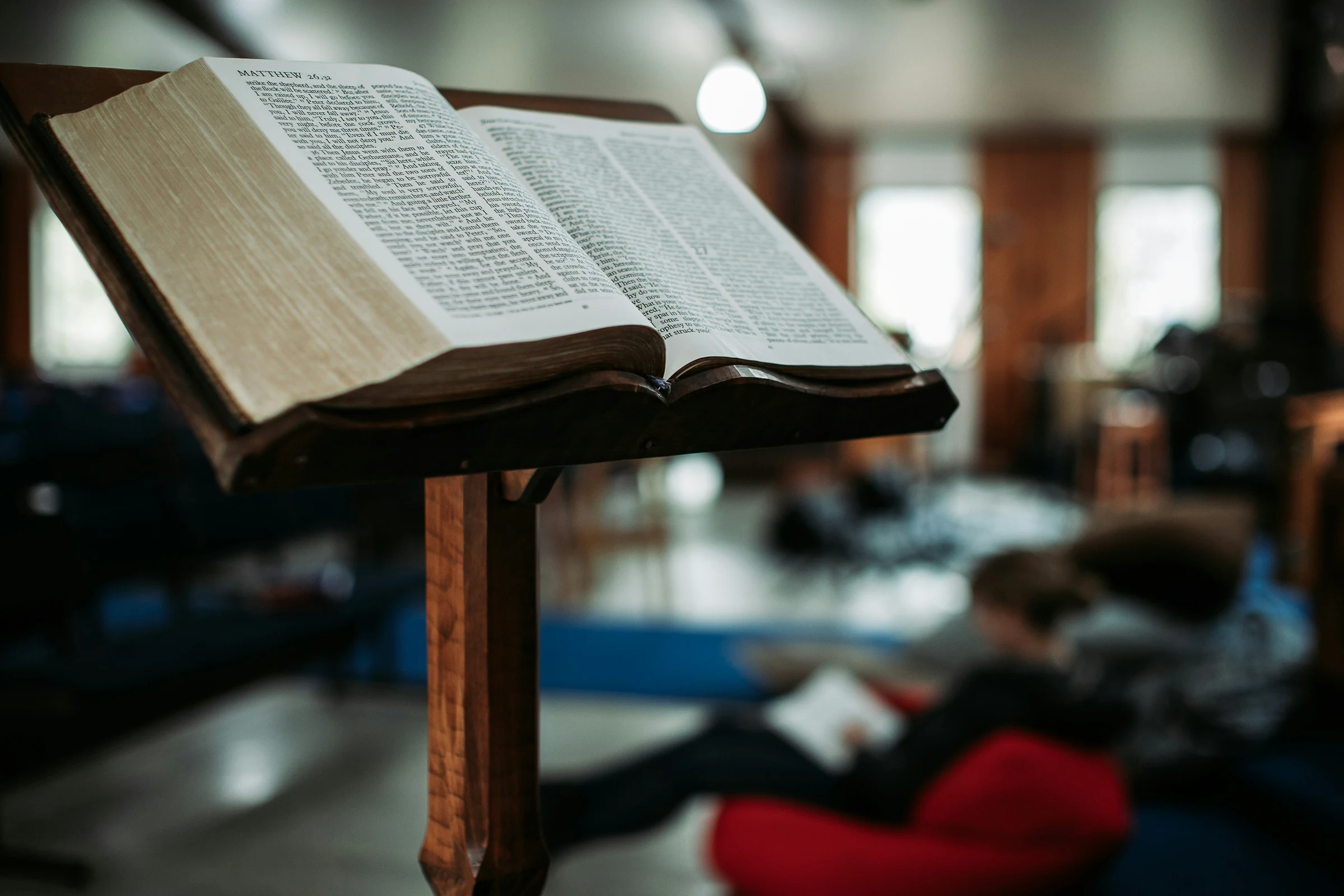 An open Bible resting on a simple wooden pulpit, warm light.